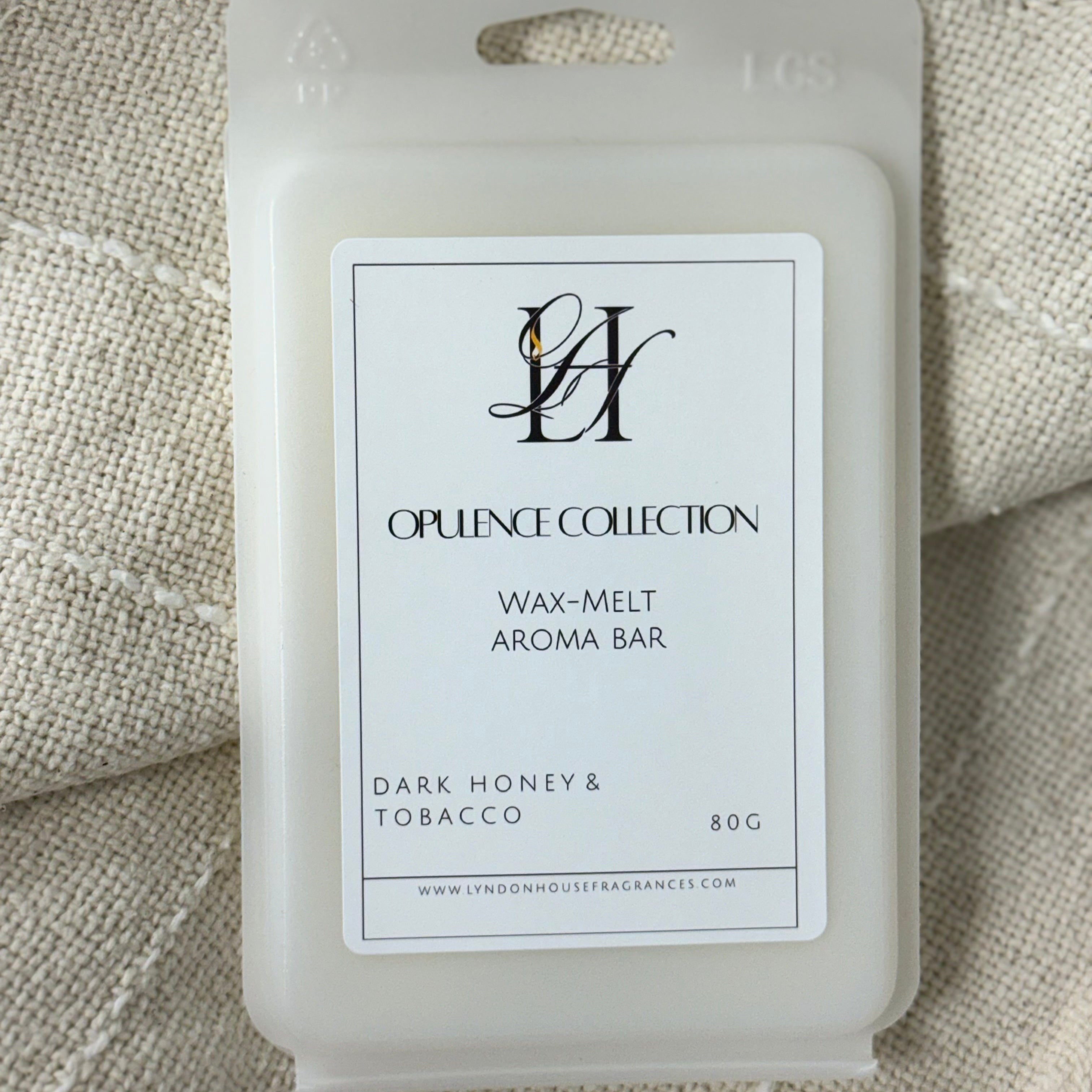 A wax melt package from tLyndon House Fragrances Opulence Collection, labeled 'Dark Honey & Tobacco' and '80G', resting on a textured beige woven fabric background.