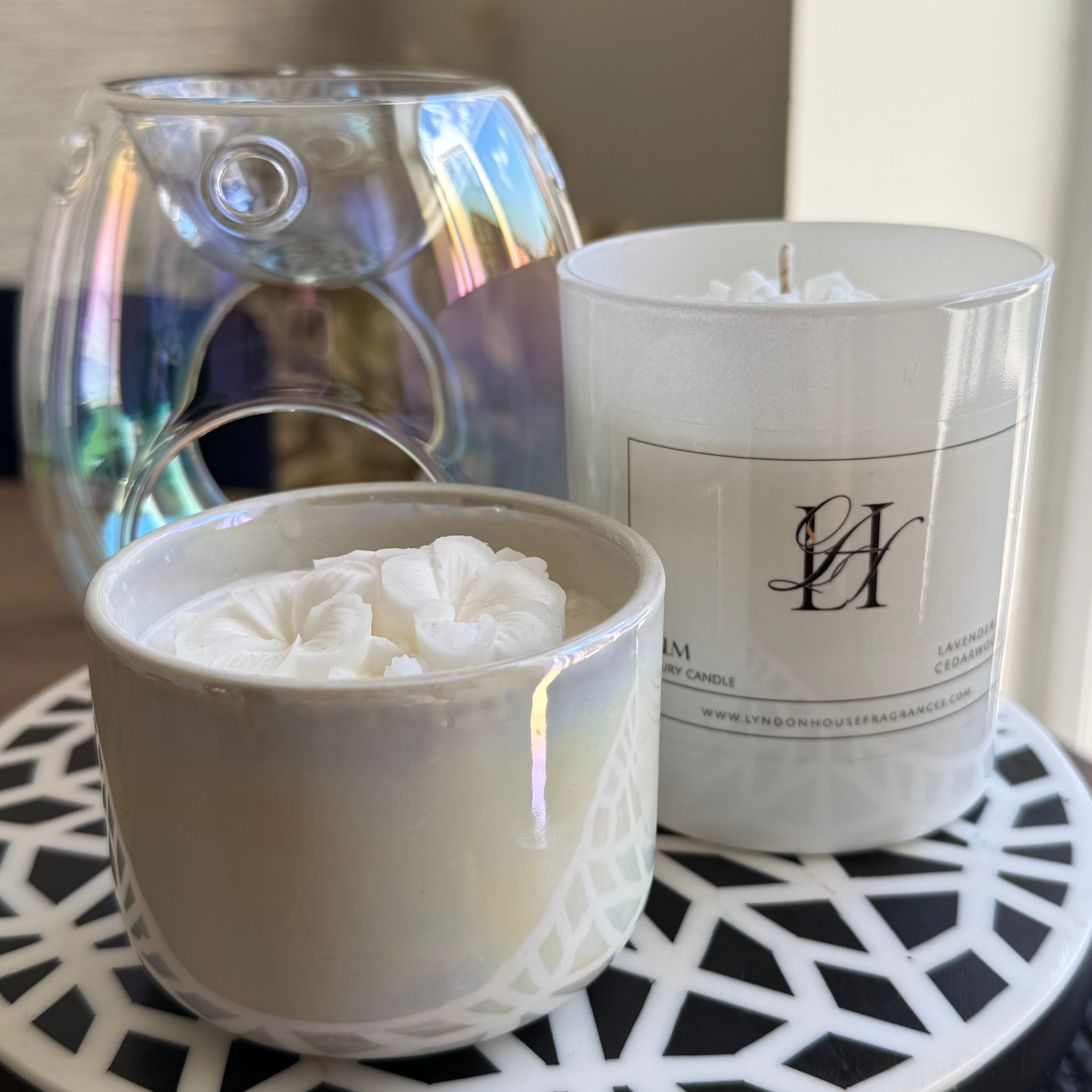 Two candles, one in a glass container and the other in a white holder with a visible brand logo, on a decorative tray.