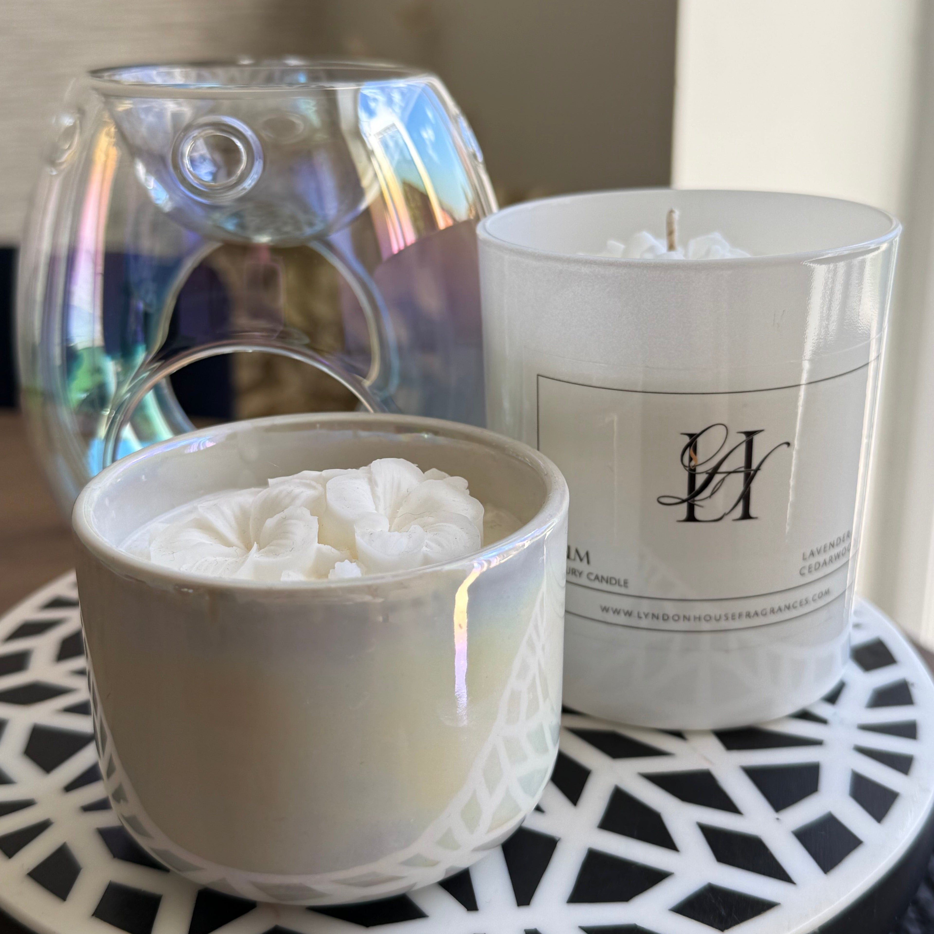 Two candles, one in a glass container and the other in a white holder with a visible brand logo, on a decorative tray.