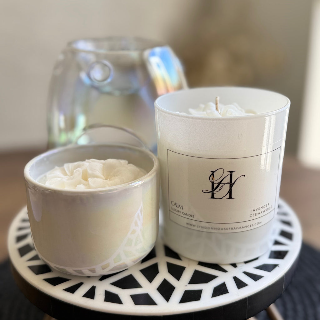 Two candles, one in a white container and the other in a decorative holder, on a small round table.
