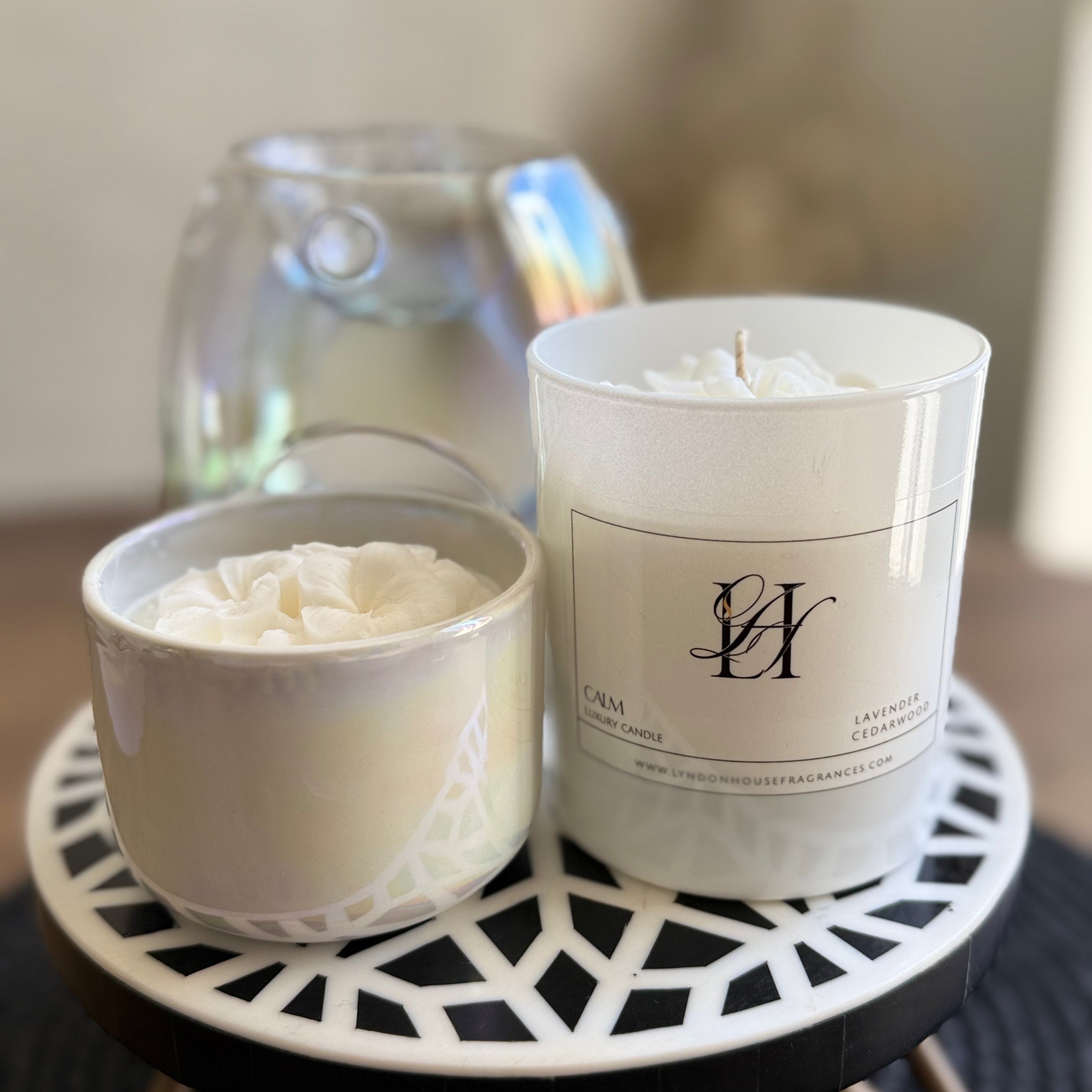 Two candles, one in a white container and the other in a decorative holder, on a small round table.