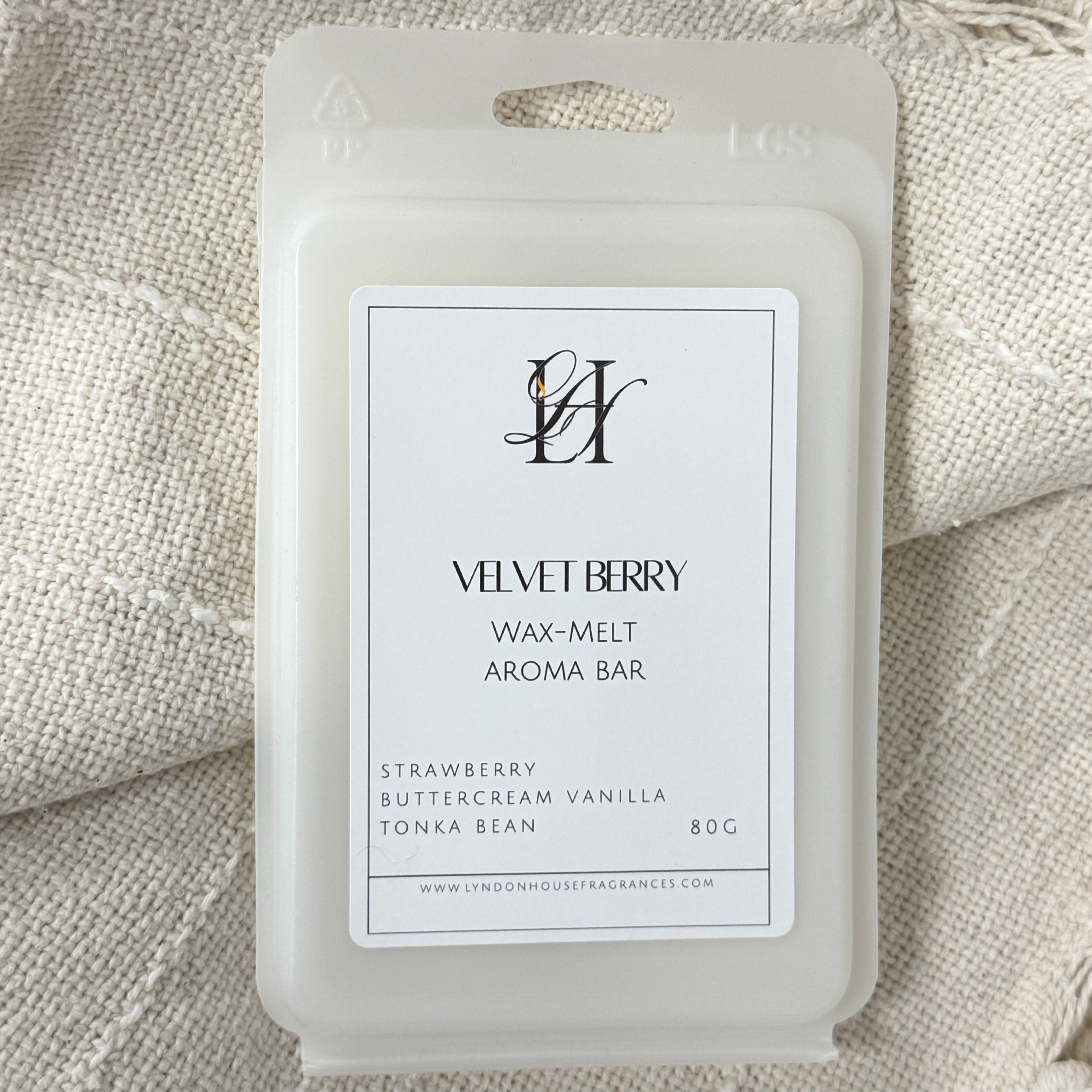 A wax melt package labeled 'VELVET BERRY WAX-MELT AROMA BAR' placed on a textured cream fabric background with tassels.